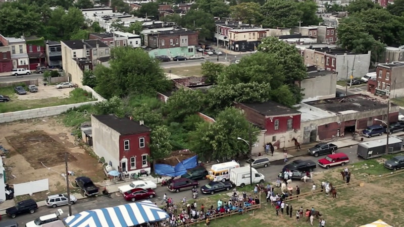 An aerial view of the Horse Day event shows rundown row houses and empty lots, illustrating the area's poverty.
