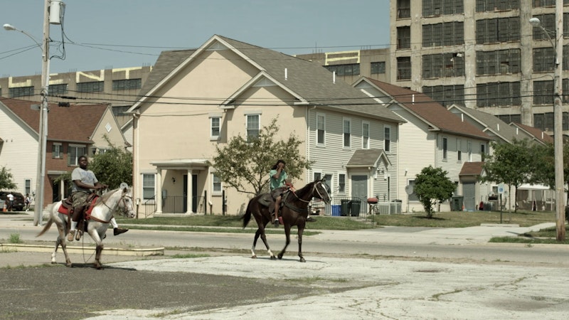 Two men ride horses through a poor area of the city.