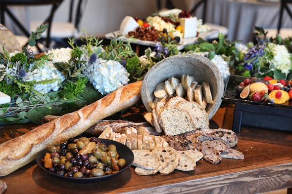 A table is topped with an attractive array of bread, olives, and fruit.